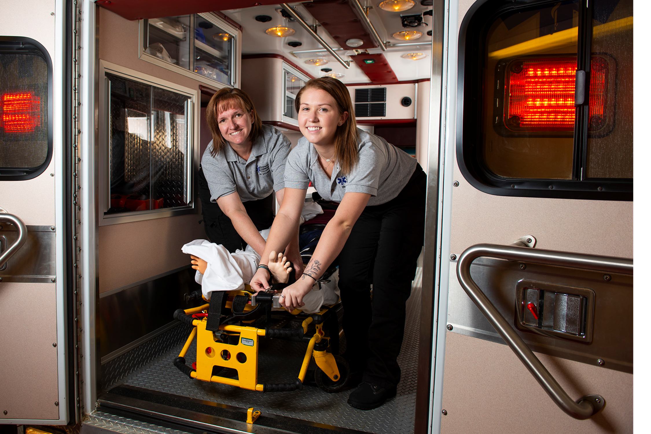 Two medical students practicing on a manikin in an ambulance.
