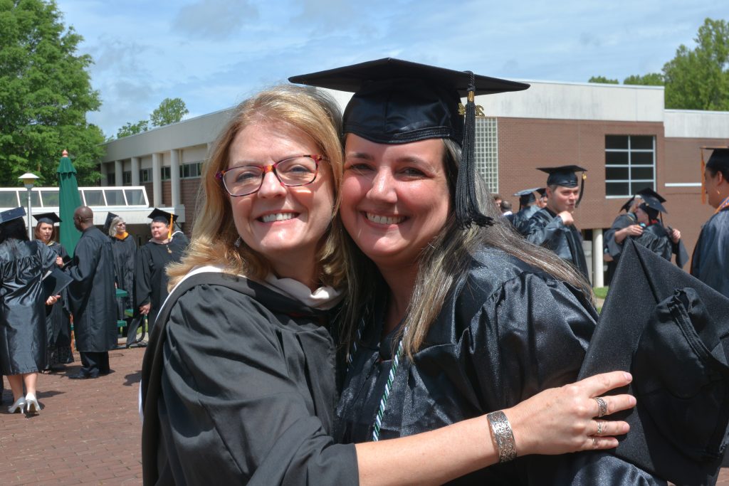 A female graduate and a female faculty member smile and hug