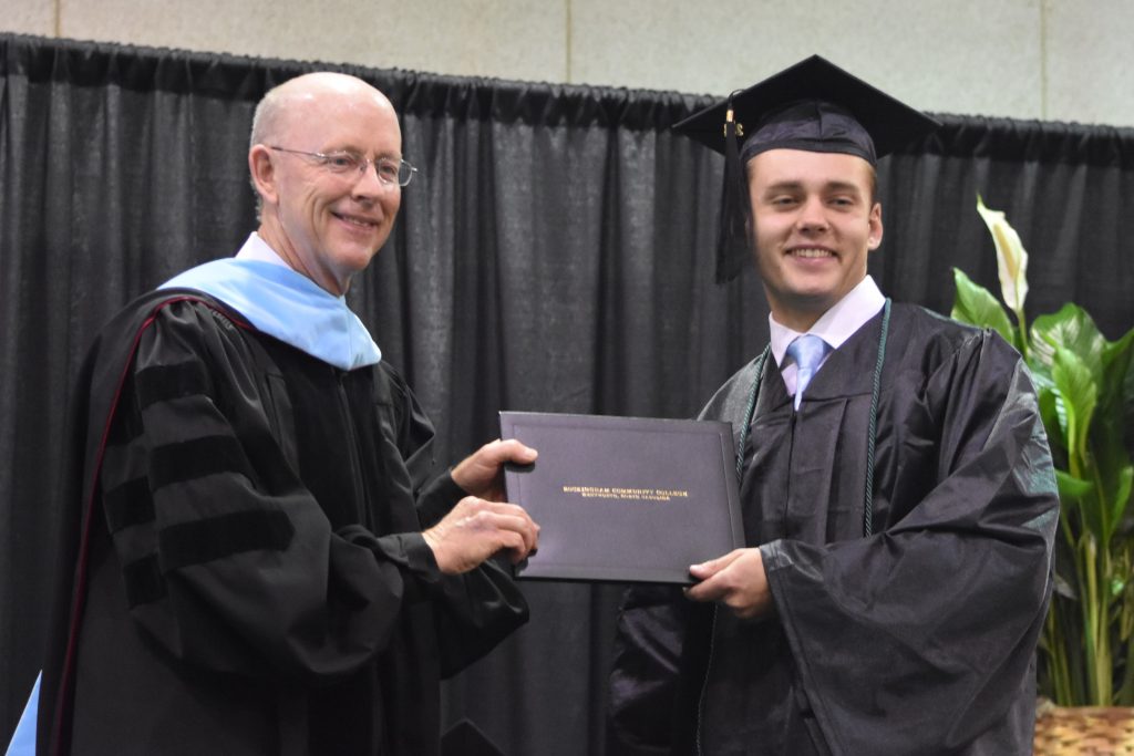 A white male graduate accepts his degree from the college president