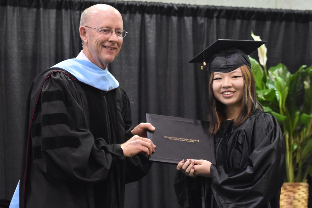 A female Asian graduate accepts her degree from the college president