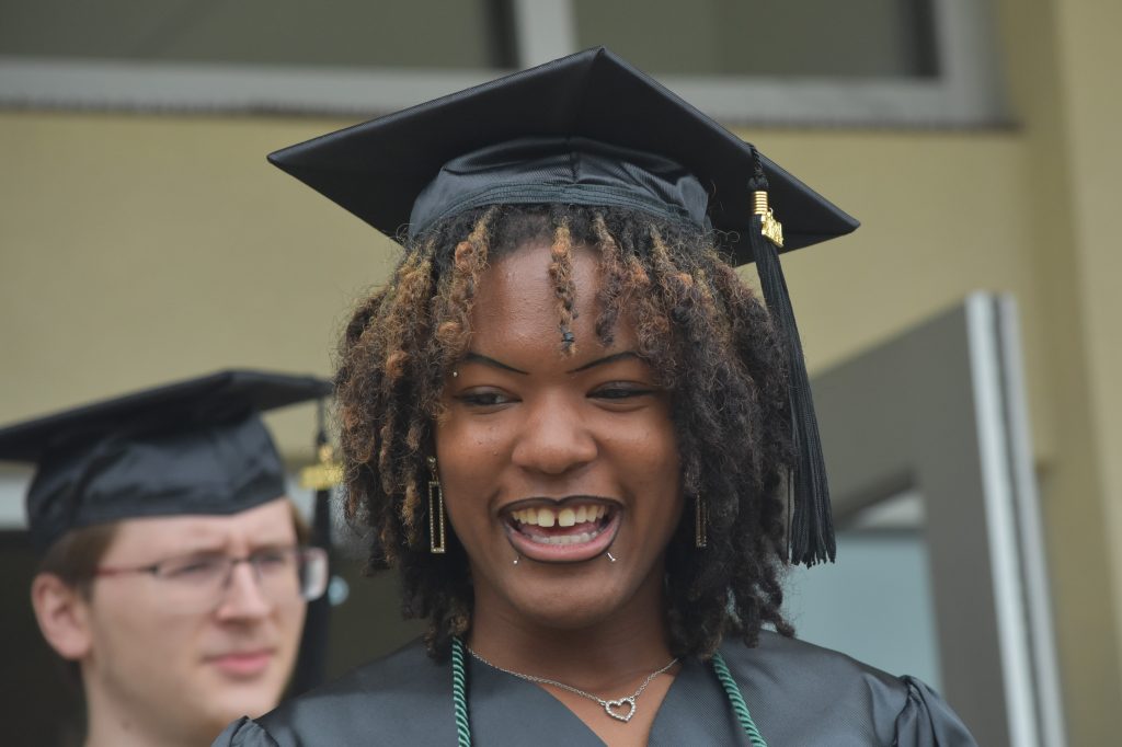 A female Black graduate smiles big as she exits the gym