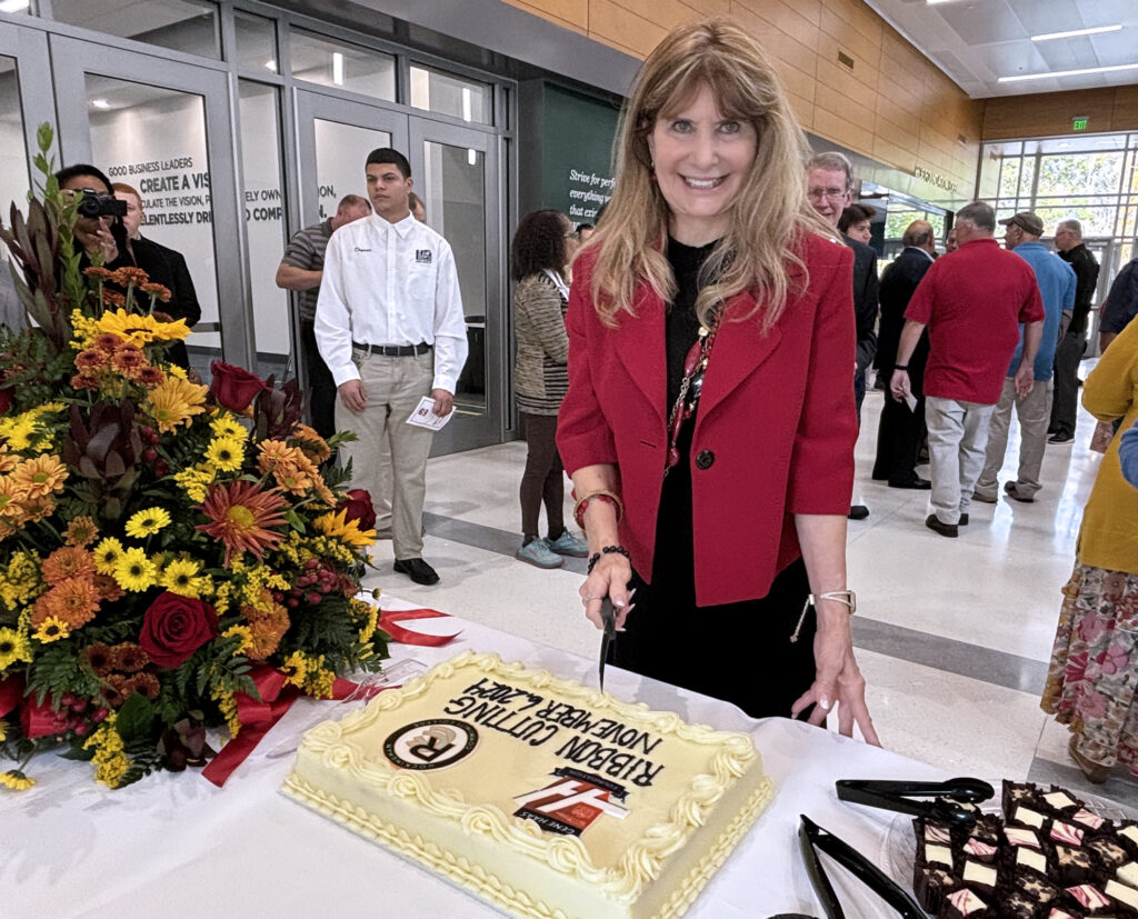 A woman holds a knife over a cake, while groups of people gather in the background talking.