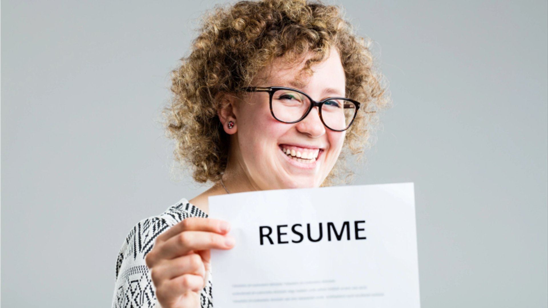 A smiling lady holds a résumé up to the camera