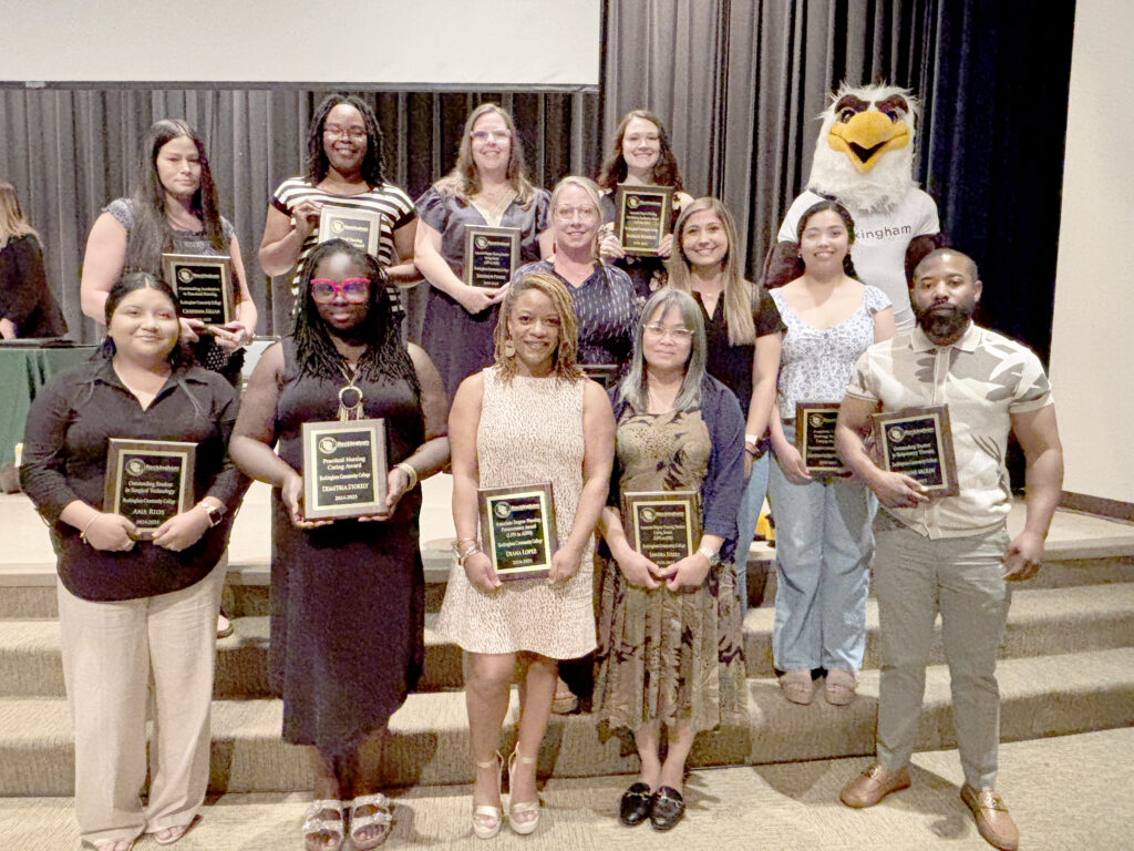 Twelve college students display plaques on a stage with an eagle mascot.