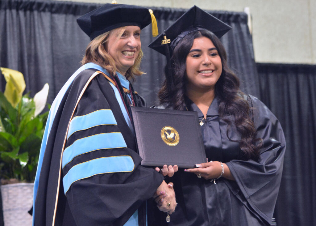 Two women shake hands and hold a diploma on stage.