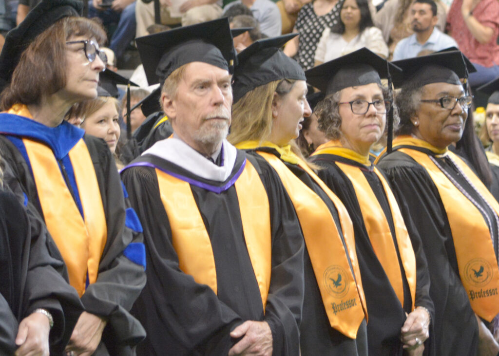 Several professors stand together in full graduation regalia during the ceremony.