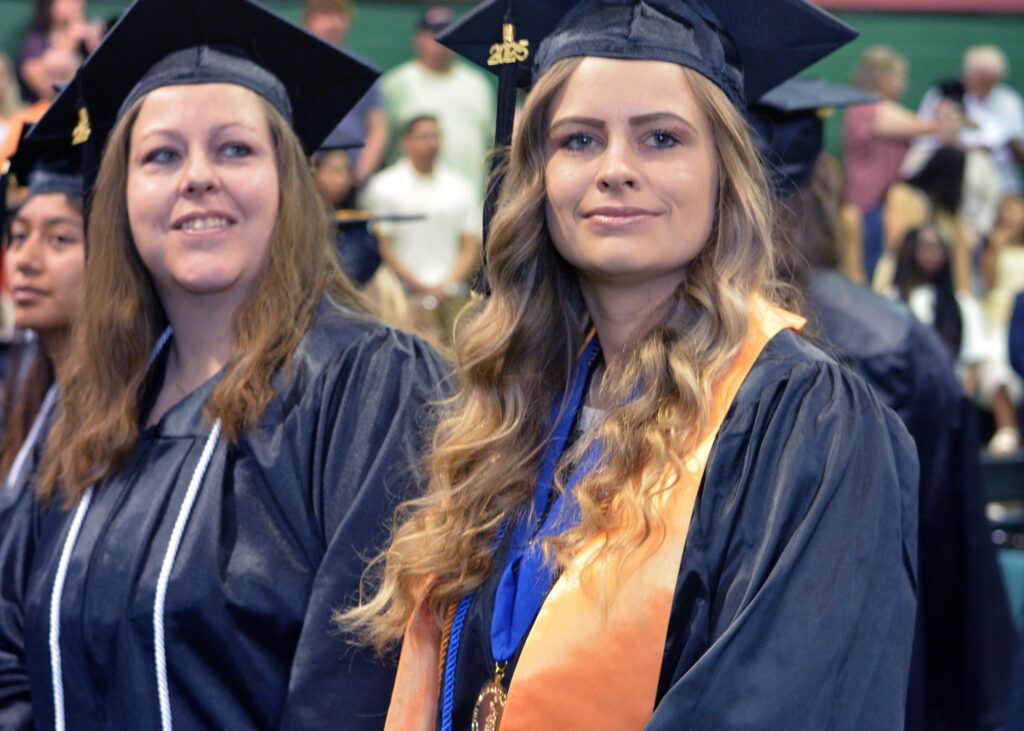 Two female graduates smile from their seats.