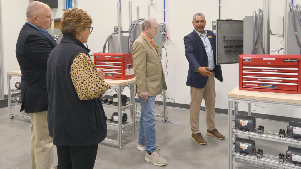 A man shows equipment in a student lab to two men and a woman.
