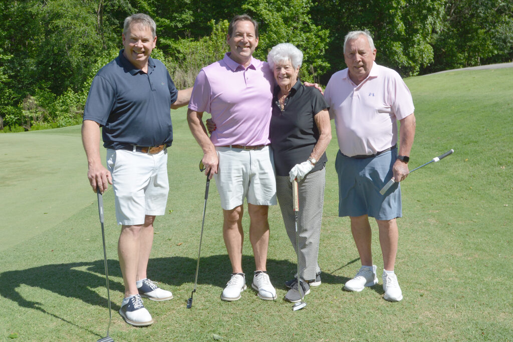 Three men and a woman smile on a golf course.