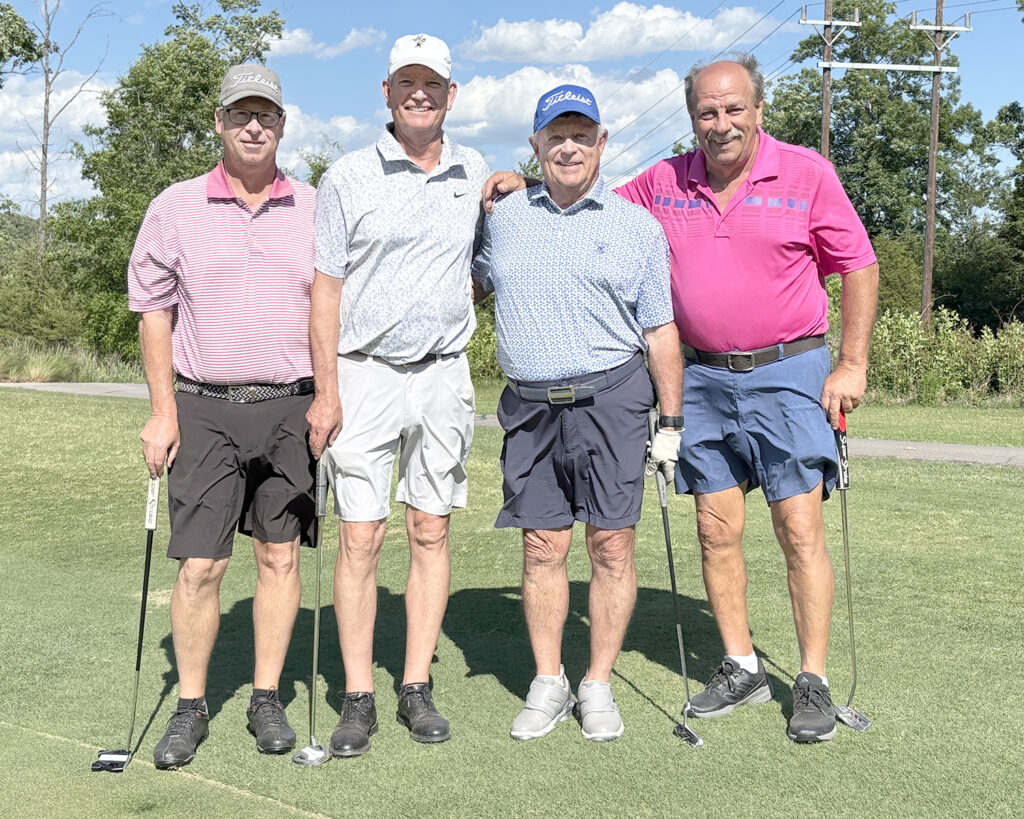 Four men smile on a golf course.