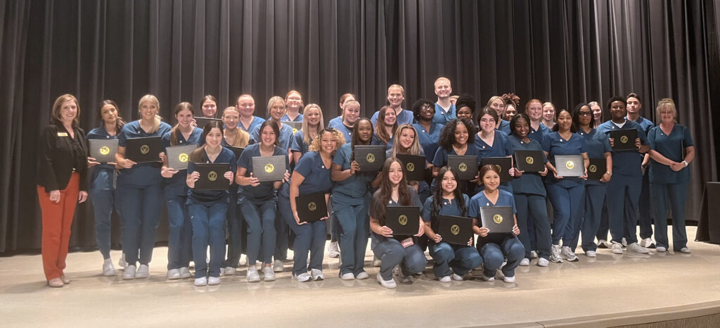 A woman and a large group of students holding certificates and smiling on a stage.