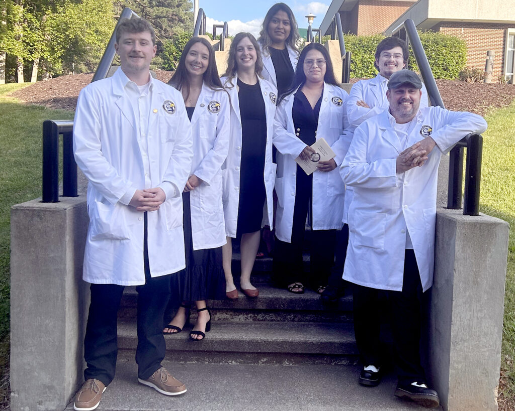 A group of smiling students in white lab coats.