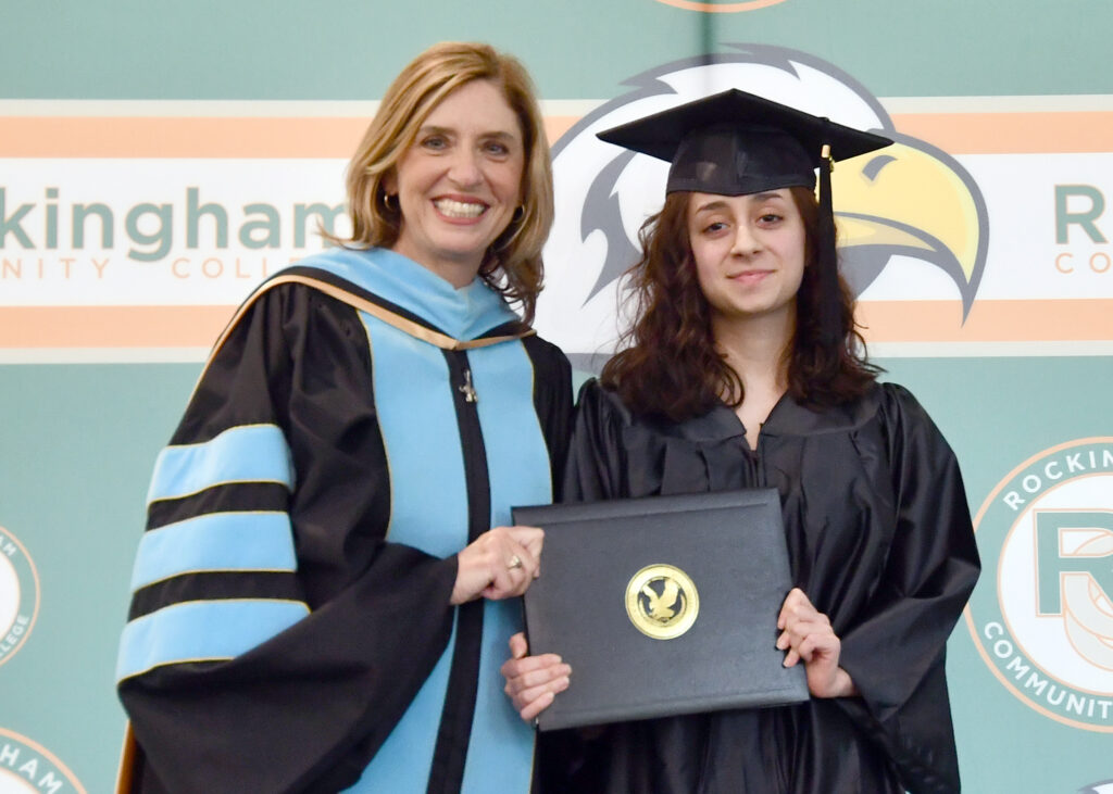 Two women smile, one in a cap and gown holding a diploma.