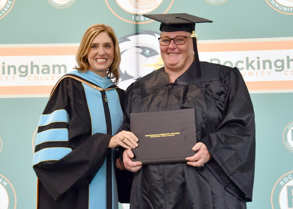 Two women smile, one in a cap and gown holding a diploma.