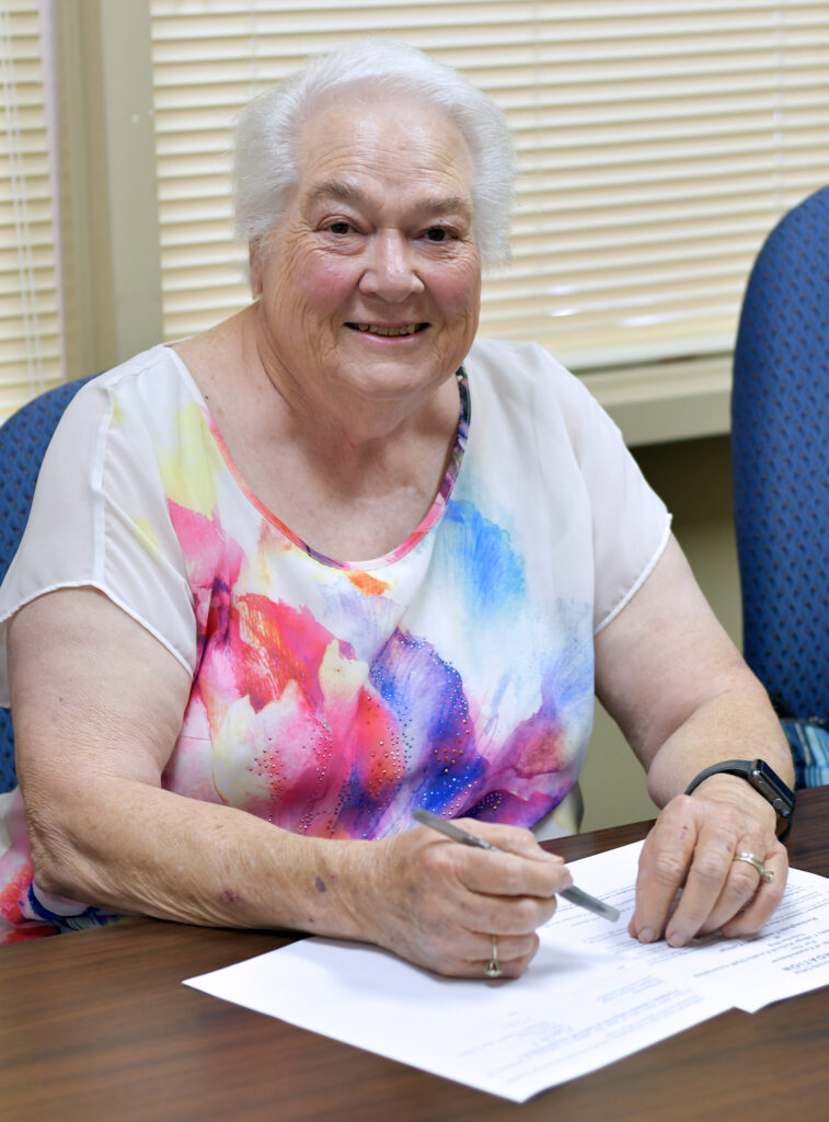 A lady smiles, sitting at a table with pieces of paper.