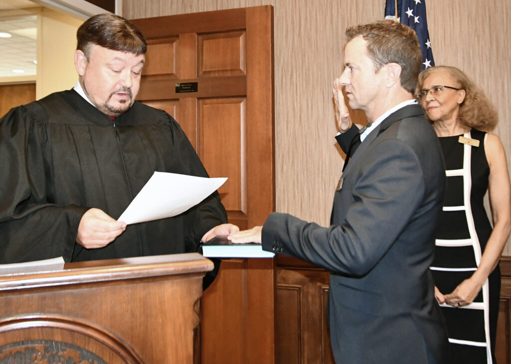 A man administers an oath of office to another man, as a woman looks on.