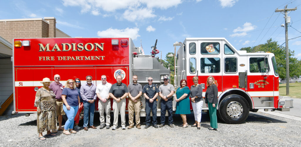 A group of people stand at the side of a large fire truck branded with Madison Fire Department.