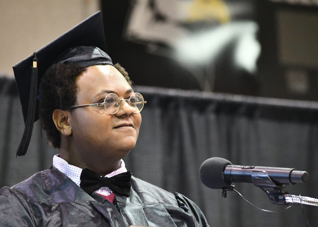 A student in a cap and gown stands at a microphone.