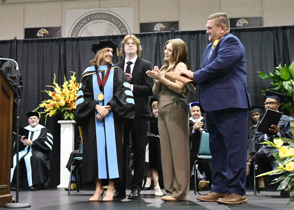 A woman looks back at her family and smiles on stage.