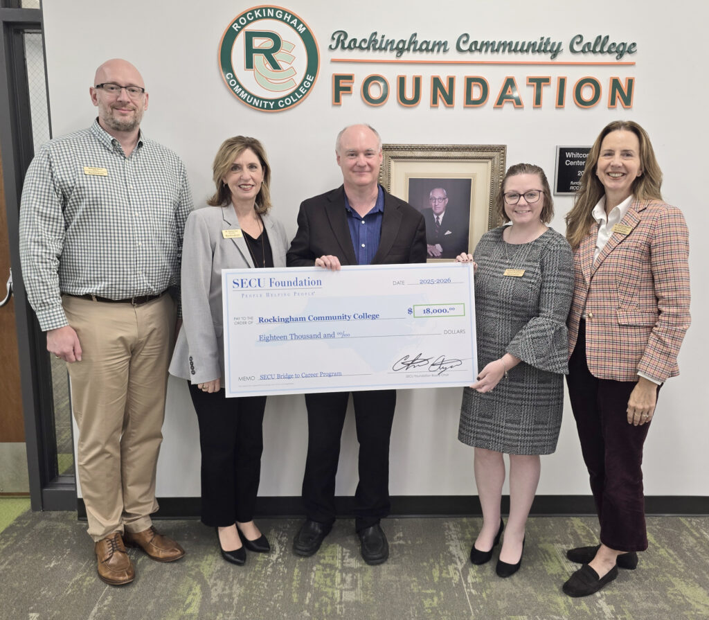 Five people hold up a large $18,000 check in front of a Rockingham Community College Foundation sign