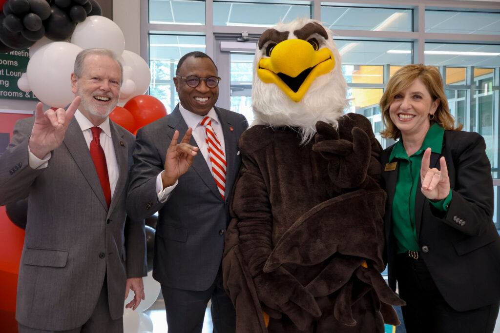 Two men, a woman and an eagle mascot make a wolfpack hand sign