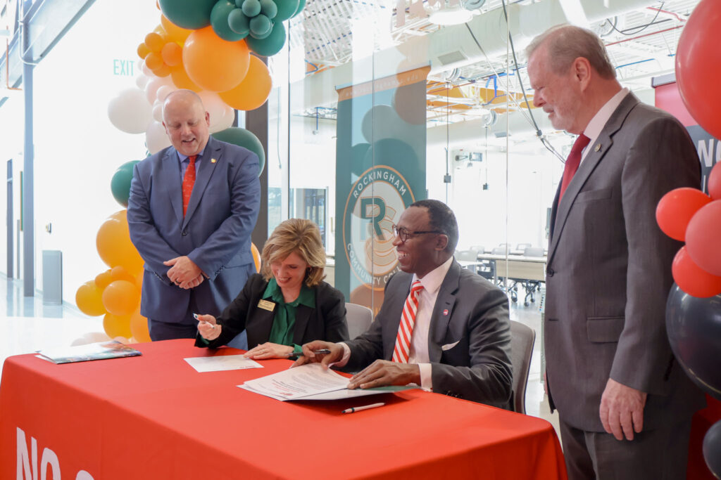 A woman signs a paper as three men look on