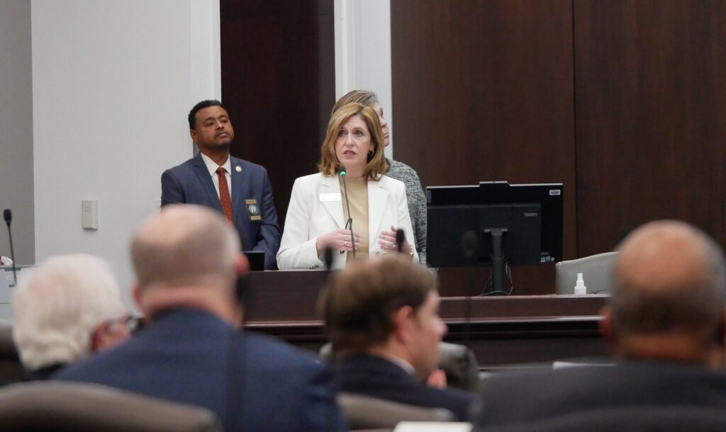 A woman talks at a microphone in front of a room full of people.