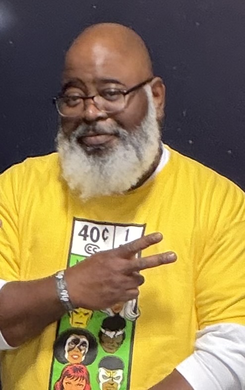A Black man in a yellow shirt with comic characters on the front.