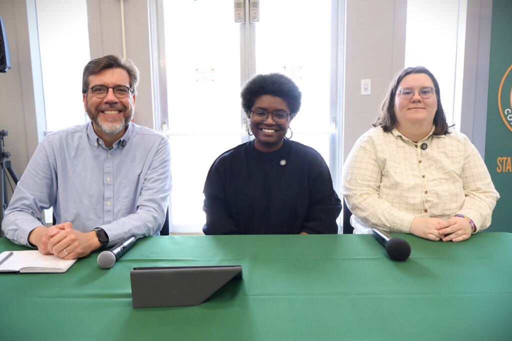A man and two women sit at a table with microphones.