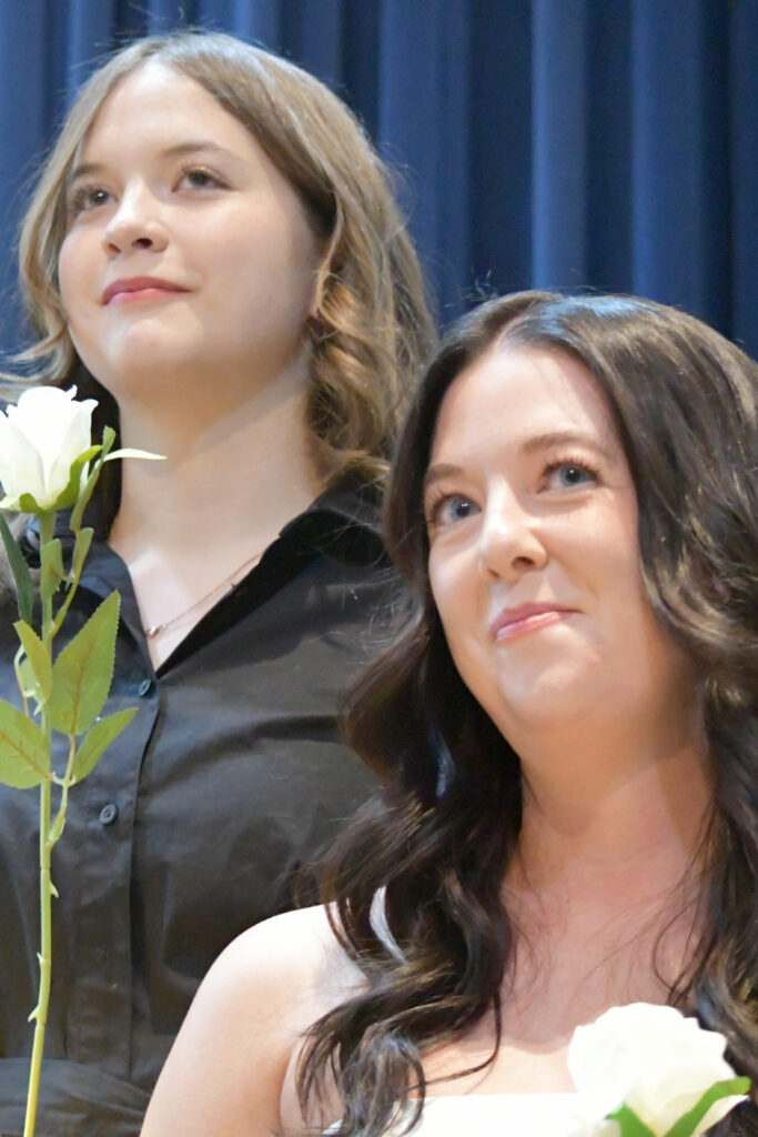 Two PTK inductees hold white roses and look out into the distance from the stage.