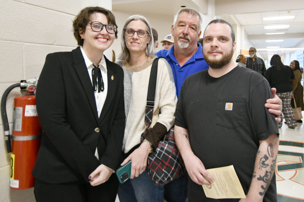 An honor society inductee wearing a new lapel pin smiles with three family members after the PTK induction ceremony.