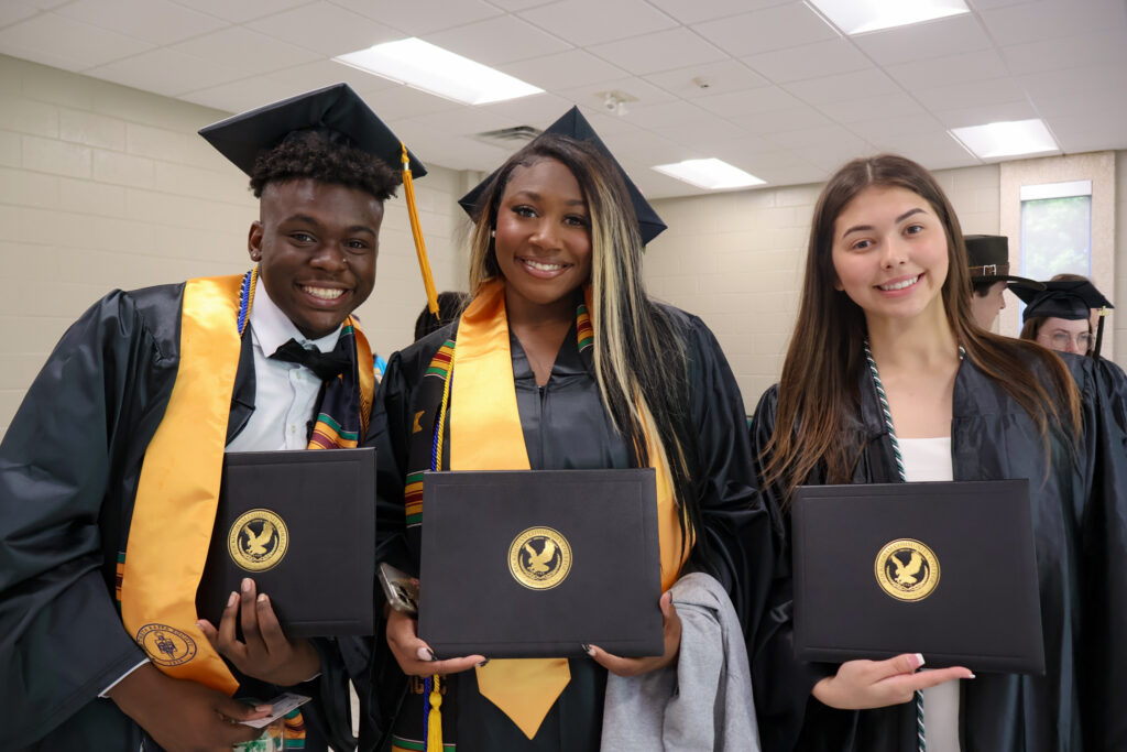 Three graduates smile with their diplomas following graduation.