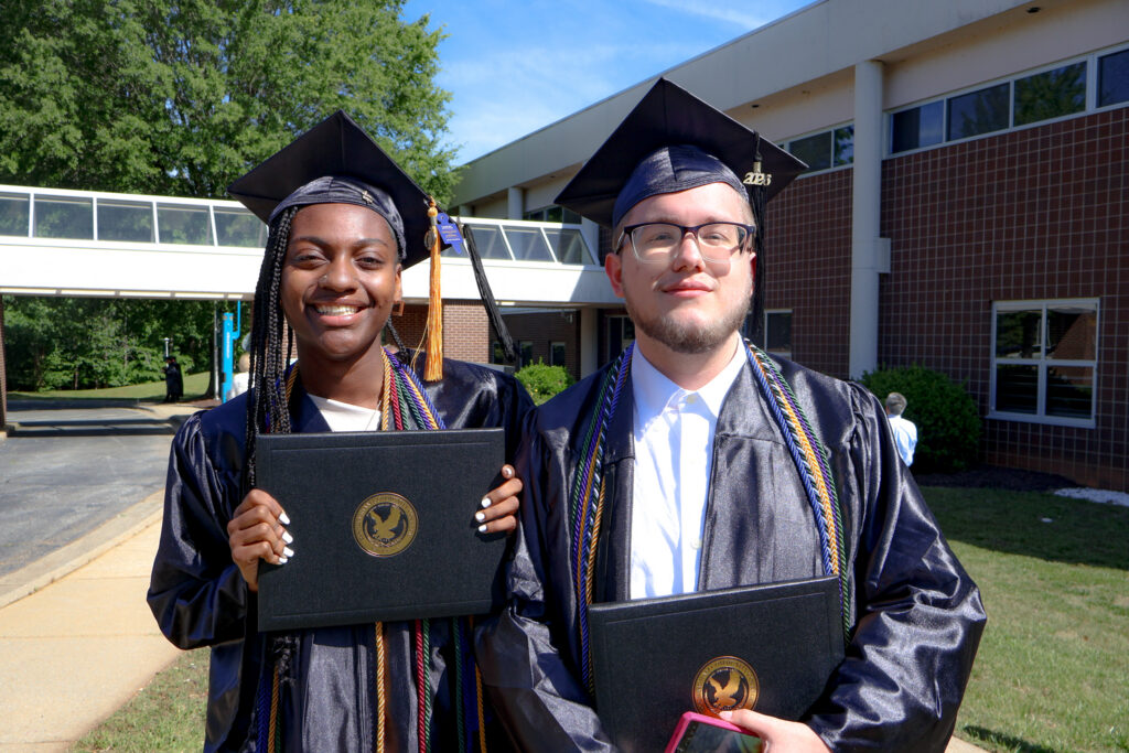 Two graduates smile with their diplomas after graduation.