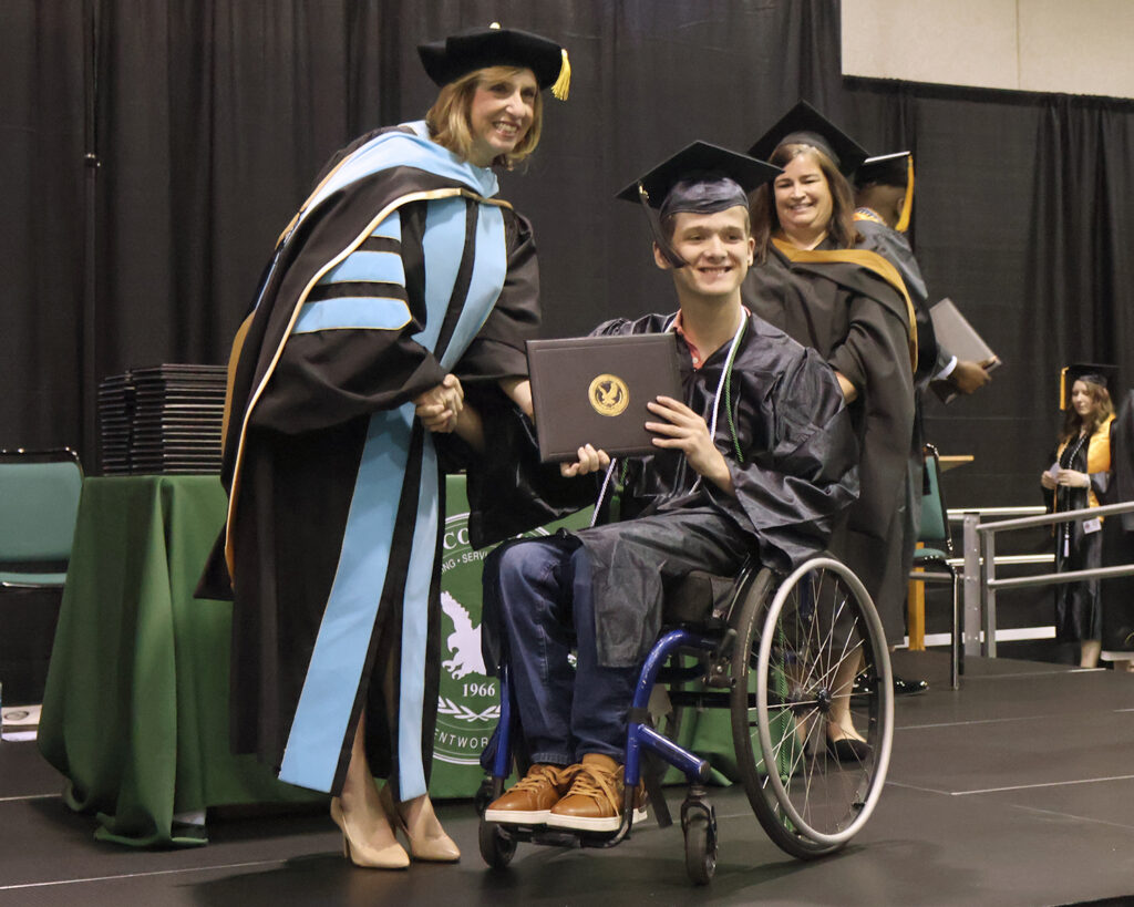 A graduate in a wheelchair accepts his diploma from the college president.