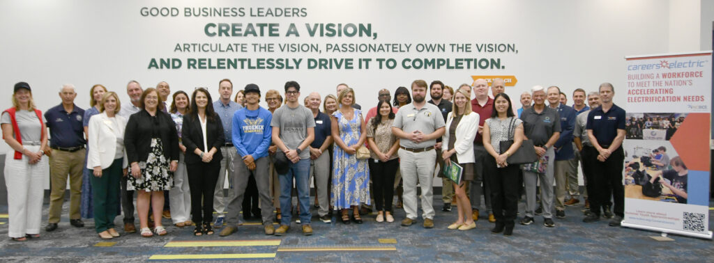 A large group of people gather beside a floor banner that says Careers Electric: building a workforce to meet the nation's accelerating electrification needs.