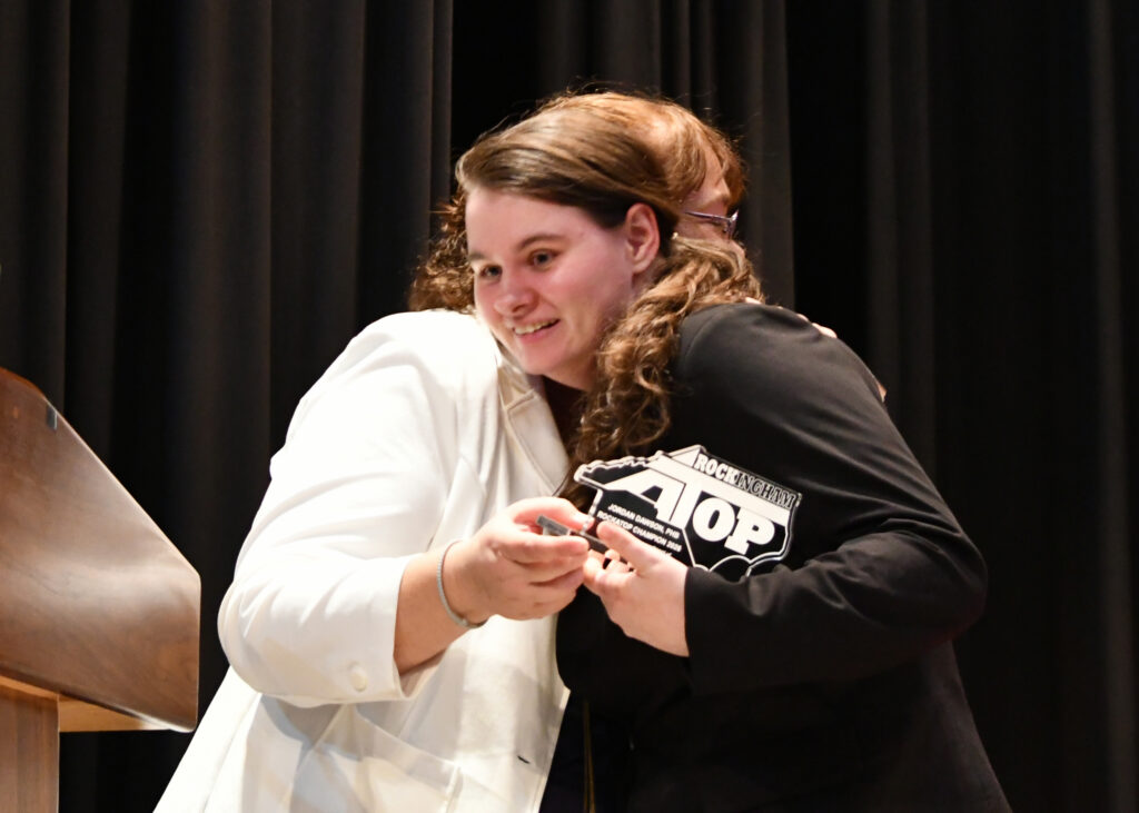 A lady hugs another on stage after accepting a RockATOP award.