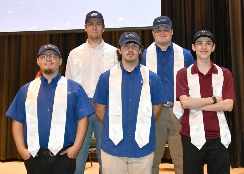Five students smile on stage after a ceremony during which the signed on as apprentices with RockATOP.