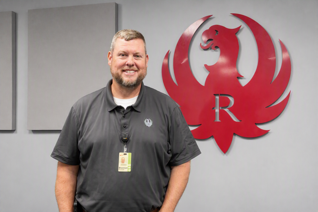 A man stands in front of a metal Ruger emblem on a wall.
