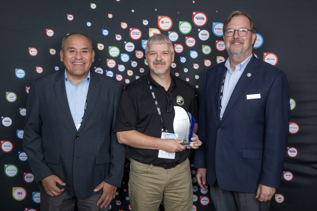 A man holds an award, flanked by two other men.